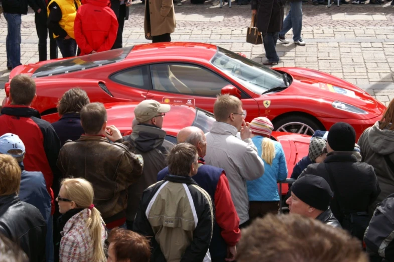 a crowd gathers around a red sports car with its hood open