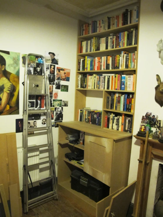 a room with a ladder, bookshelf, and pictures in the background