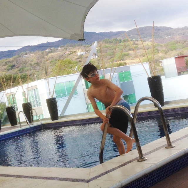 a young man standing in front of a swimming pool next to a white umbrella