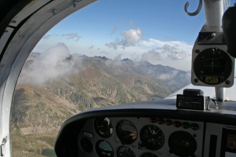 an airplane cockpit with some clouds and mountains in the background