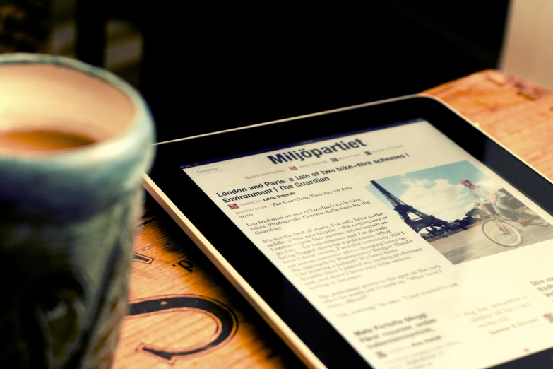 an electronic tablet sitting next to a cup of coffee