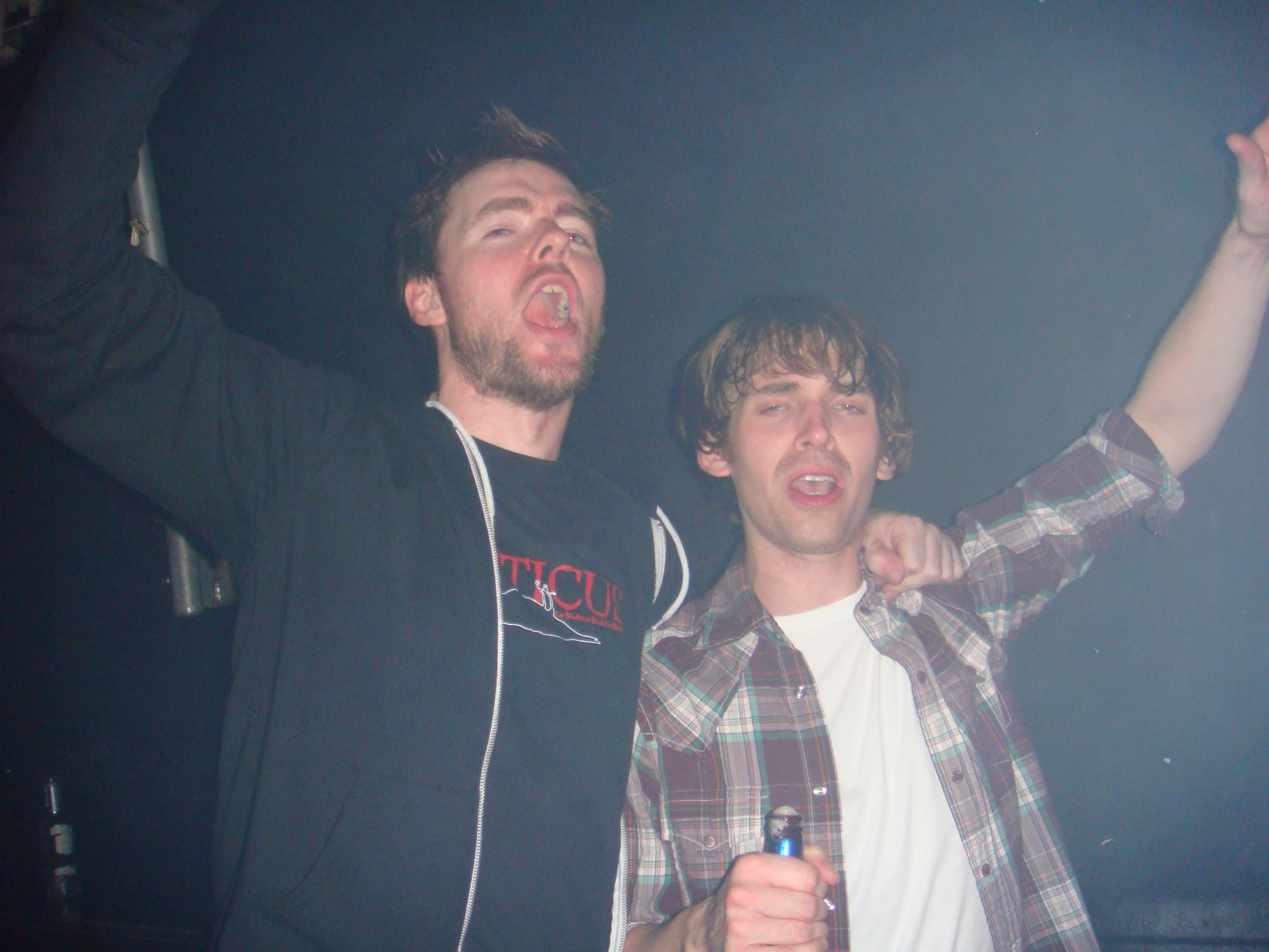 two young men are standing together with one is holding a beer