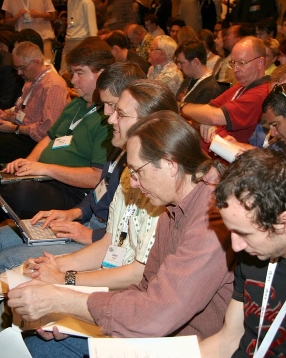 many people sit in a large room with their laptops open