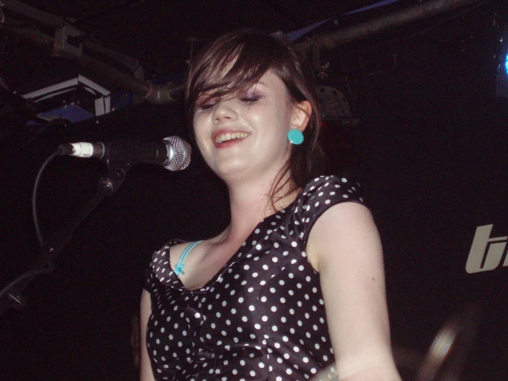 a woman with black and white dots on her dress standing in front of a microphone