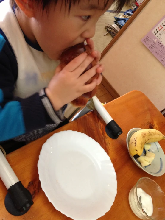 the small child eats a slice of banana in front of two empty bowls