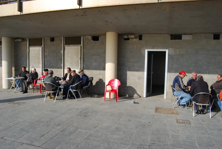 people sitting in chairs next to the building with concrete walls