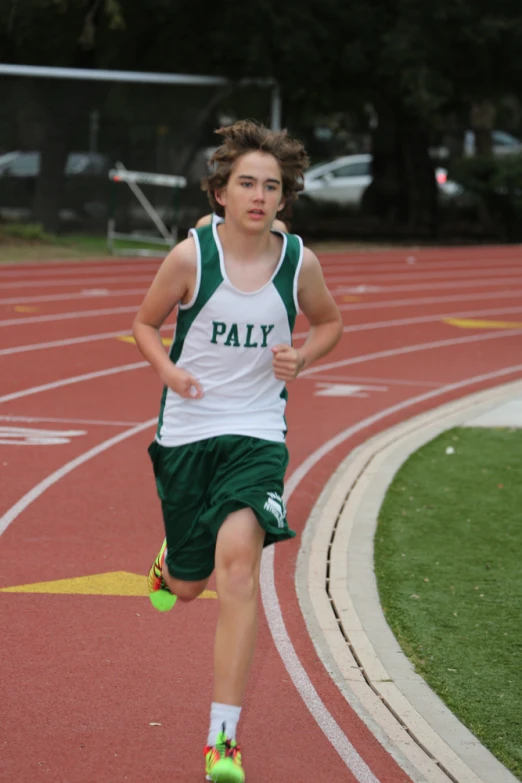 a boy in a white tank top and green shorts running on a track