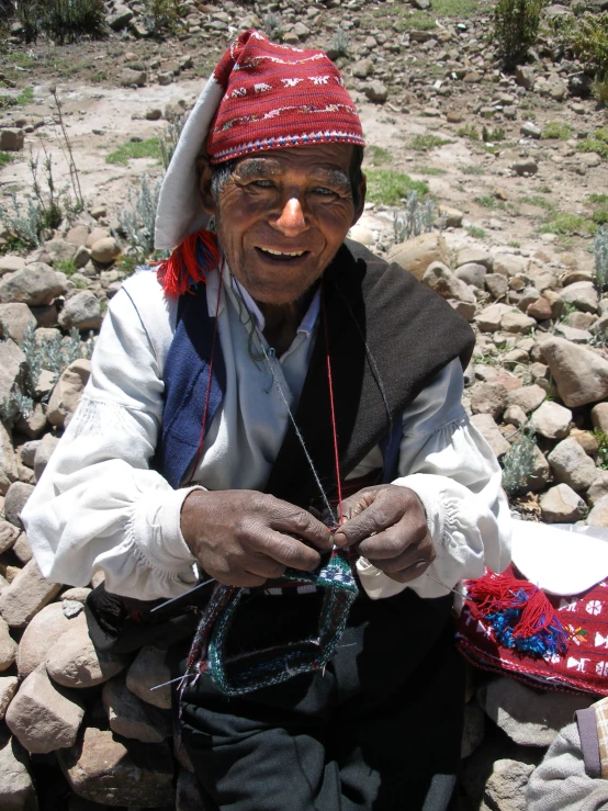 an old man sitting on rocks knitting a hat