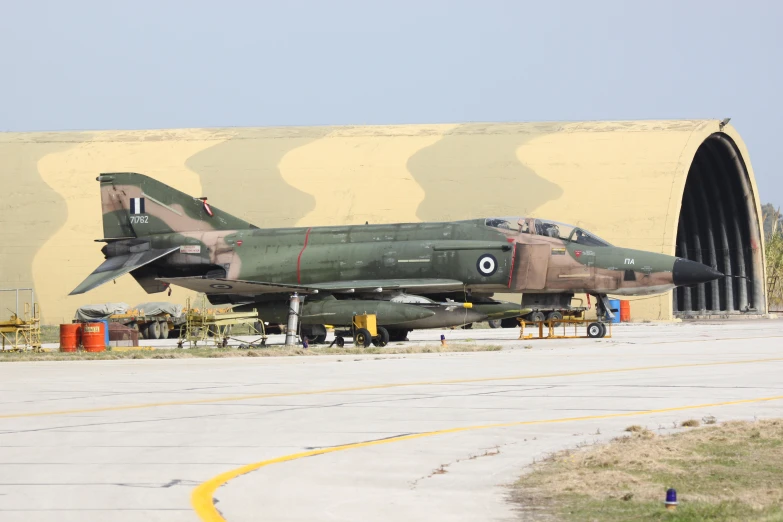 large green and tan fighter jet sitting on top of an airport runway