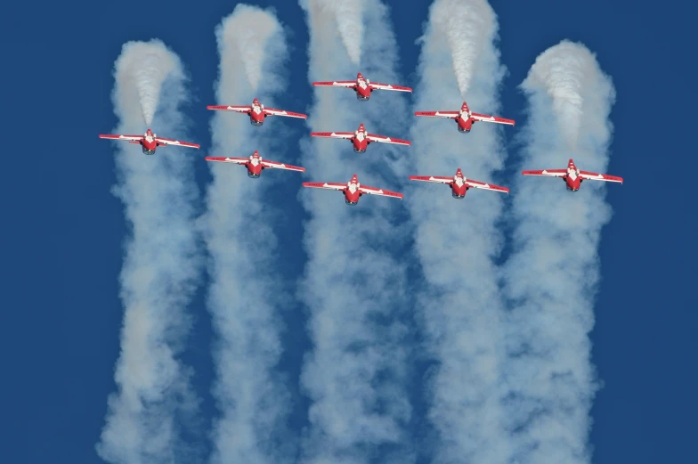 six planes flying through blue sky while leaving smoke behind them