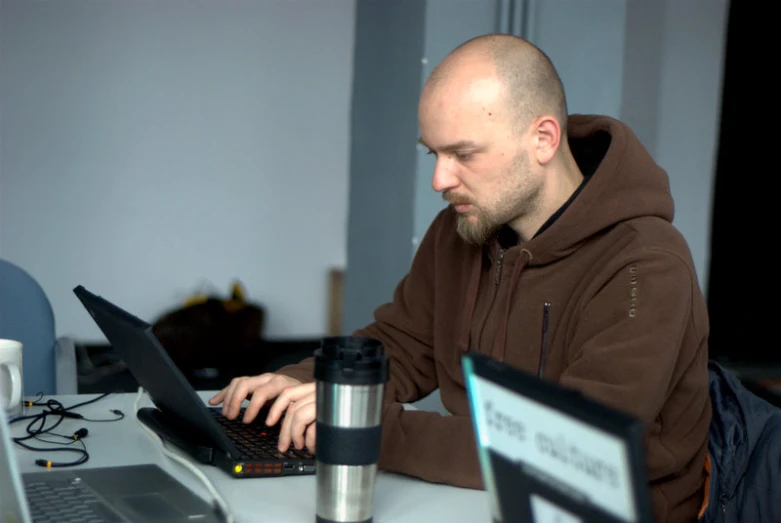 a balding man sitting at a desk working on a laptop