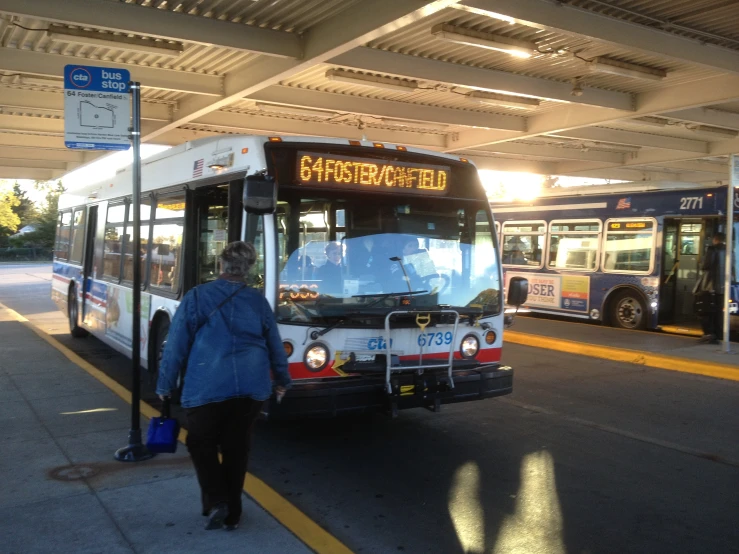 a city bus parked at the bus stop with a woman walking towards it