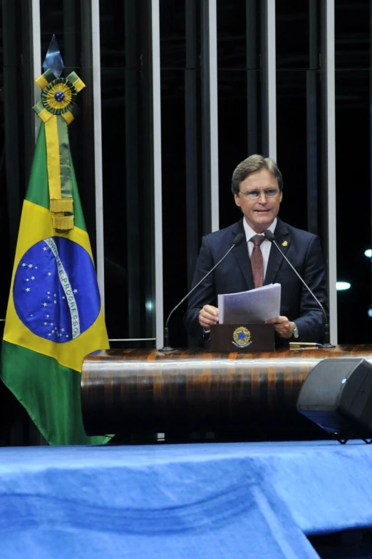 a man is speaking at a podium with two flags behind him