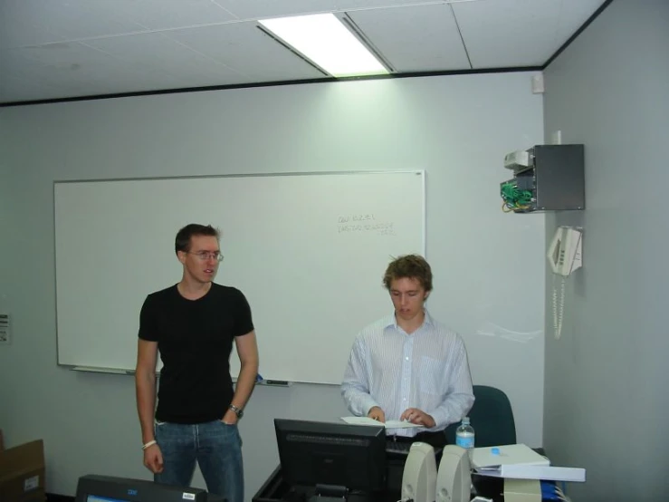 two men in an office with an white board