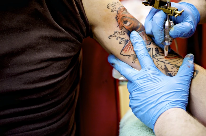 a tattoo artist getting a black piece tattooed on his arm