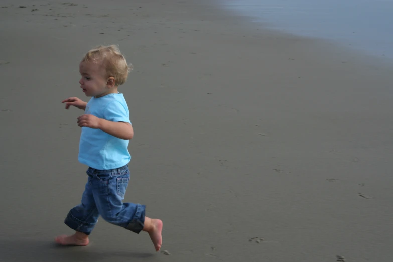 a baby running on the beach in sandals