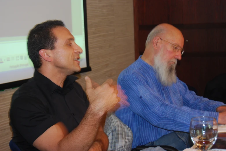 two men sitting at a table in front of a screen