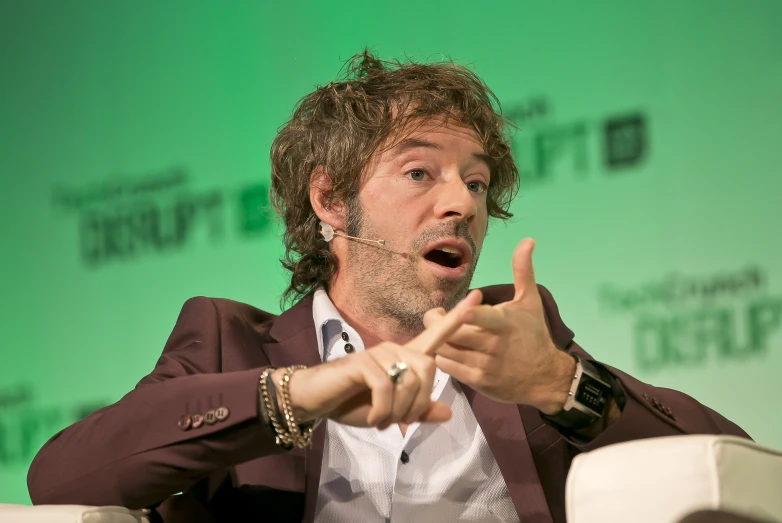 a man pointing at the camera while wearing a brown suit