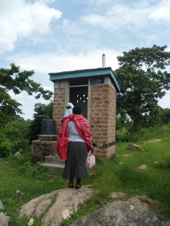 the woman stands outside of the small stone shed