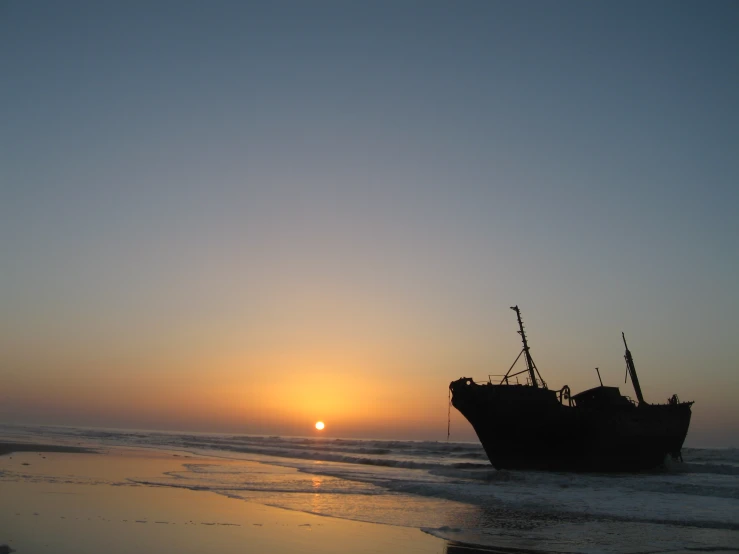 a boat sitting on top of the beach at sunset