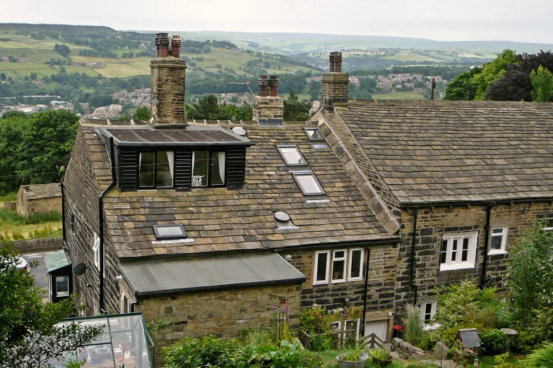 a stone and brick building with two chimneys, overlooking a field