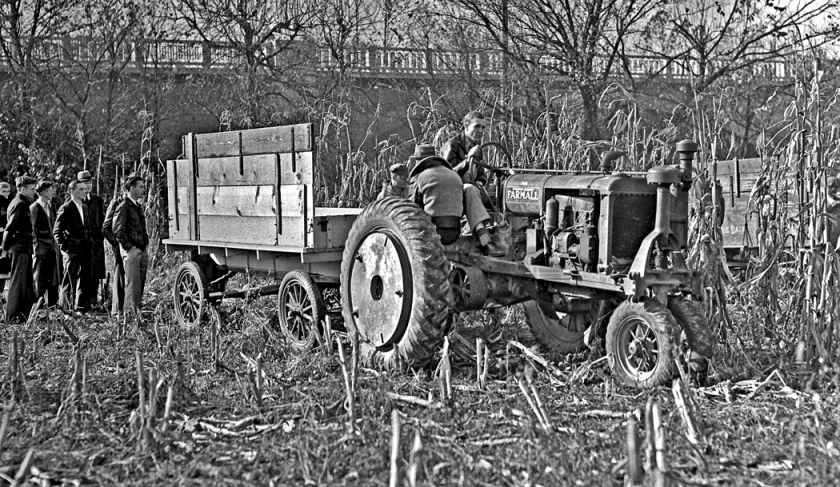 an old fashioned tractor in a field with a few men around it