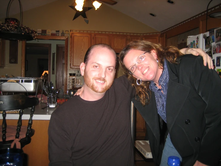 a couple poses together in their kitchen with a refrigerator and sink in the background