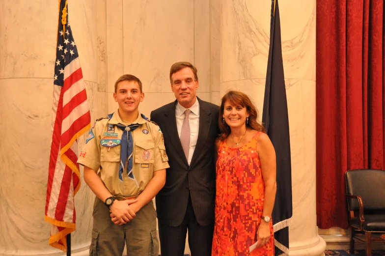 man, woman and soldier pose together in front of two flags