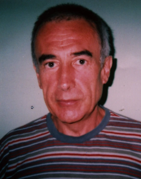 a man with a red, white and black shirt is staring directly into the camera