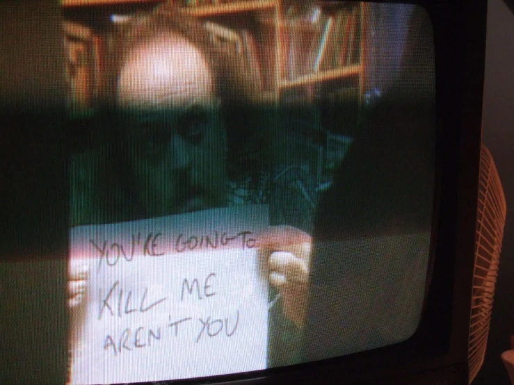 a tv screen with someone holding up a handwritten sign