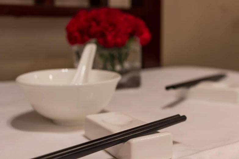 two chopsticks on the edge of a bowl and a white plate with a knife