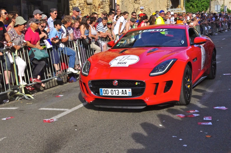 a very bright red car driving past a crowd