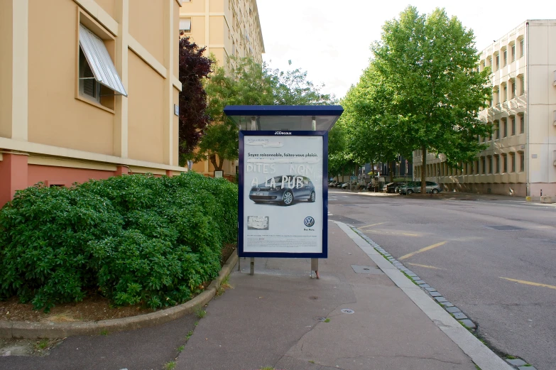 a sign for a town is beside a sidewalk with bushes