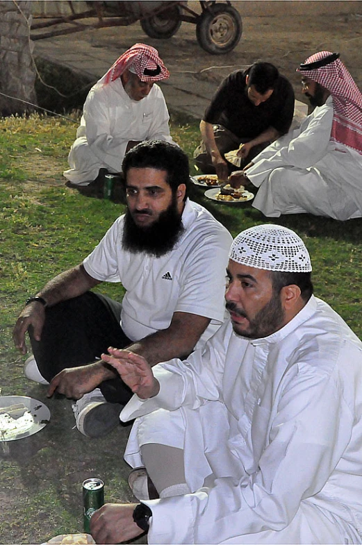 three men in white sit on the ground next to each other