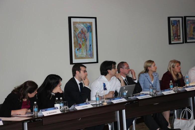 a panel of people sitting at a table listening to speakers