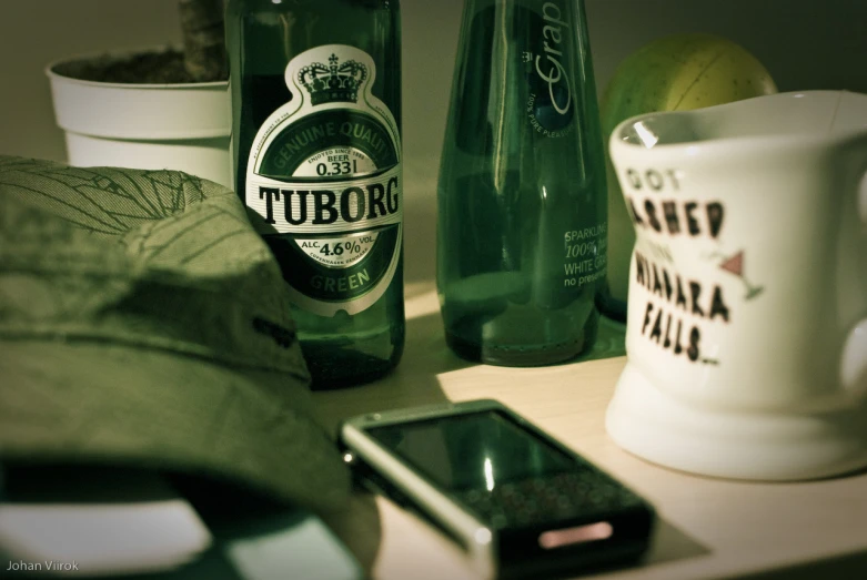 the green bottle is sitting on the desk next to the cellphone