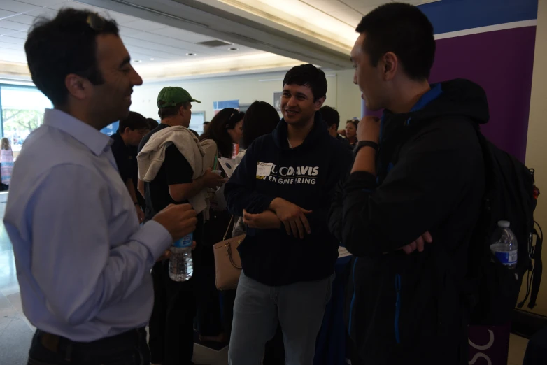 two men talking and standing around with people gathered