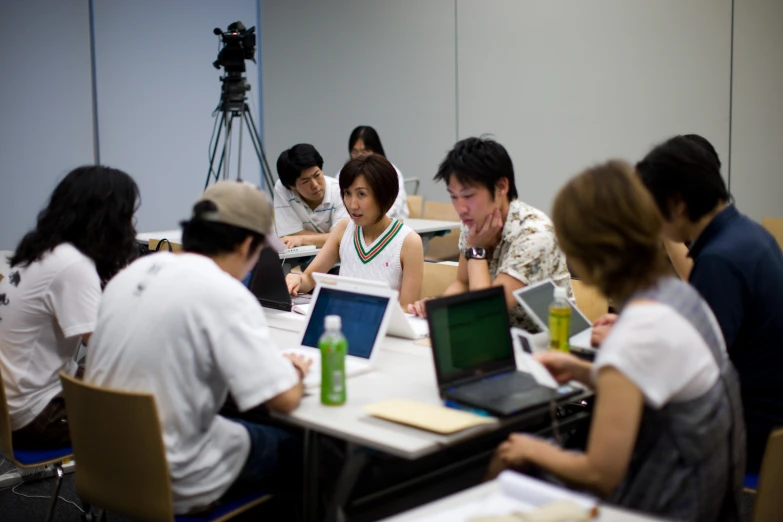 a group of people sitting around tables with laptops