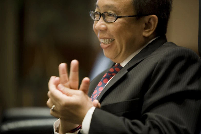 an asian man in glasses and a red tie gesturing to soing