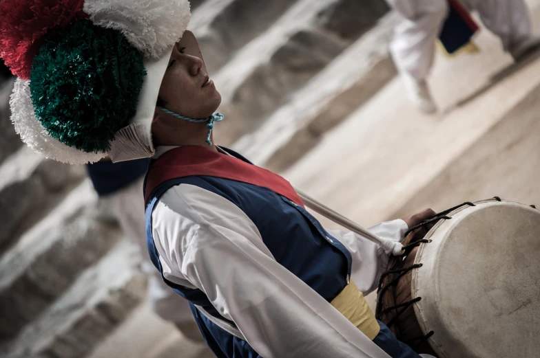 an asian drum player dressed in a red, green, white and blue costume