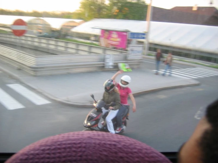 two people on a motorcycle near a bus station