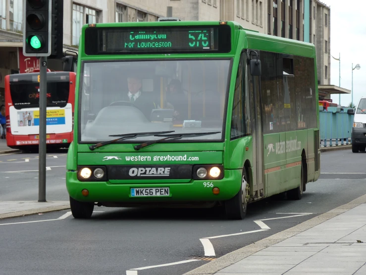 a green bus driving down the road next to a stop light