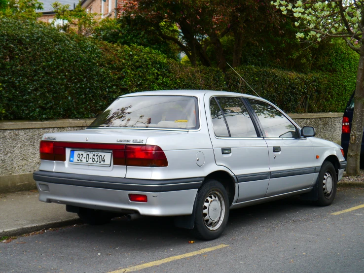 a silver parked car next to a curb with trees