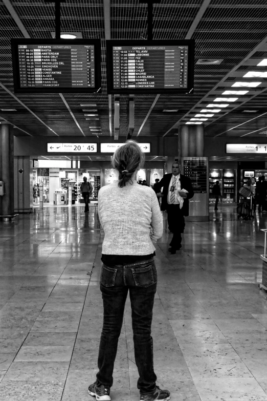 a woman in a large airport looking out at the departure boards