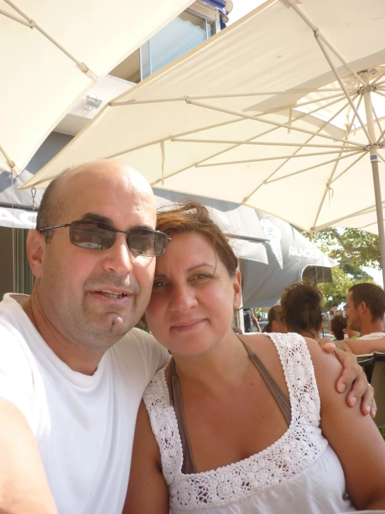 man and woman wearing sunglasses pose for a po under an umbrella