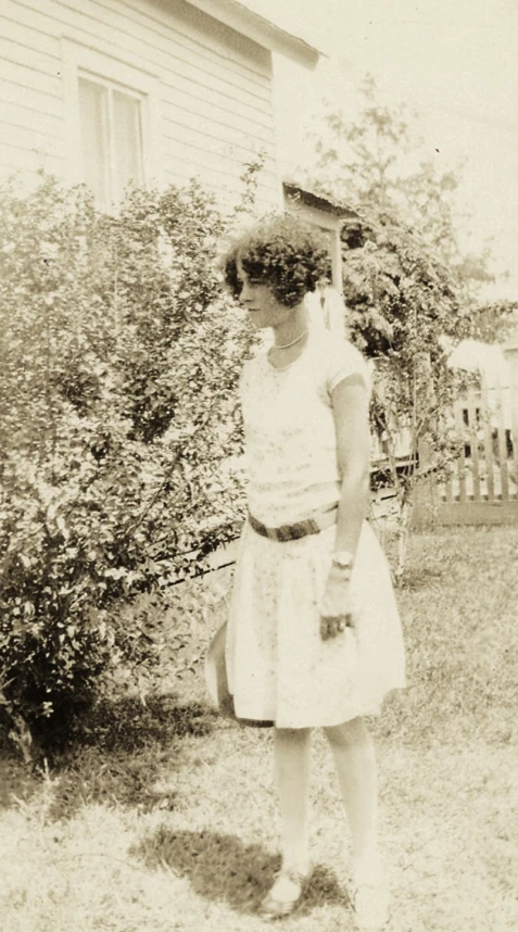 black and white pograph of woman wearing a dress in front of a house