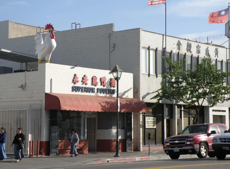 a chicken stands on top of a building near the sidewalk