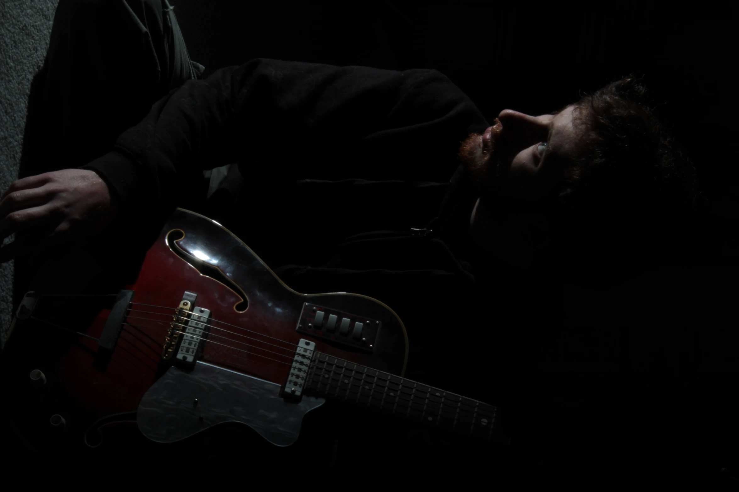 the guitarist poses with his red guitar in the dark