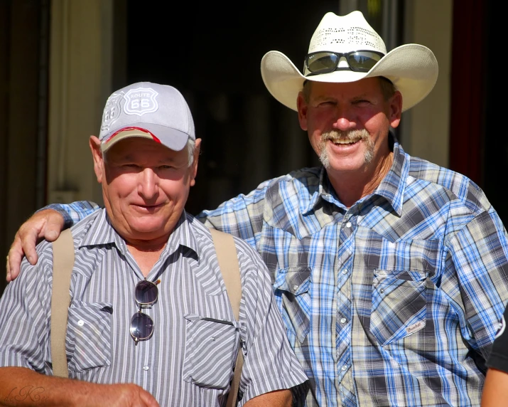 two men, one in a blue and white plaid shirt, one in a gray and white hat with a cameraman's necktie