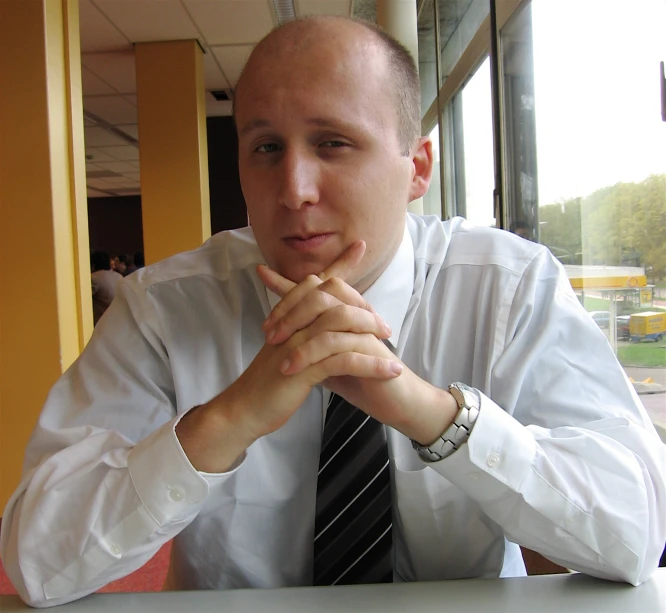 the man is sitting at the table in his white shirt and tie